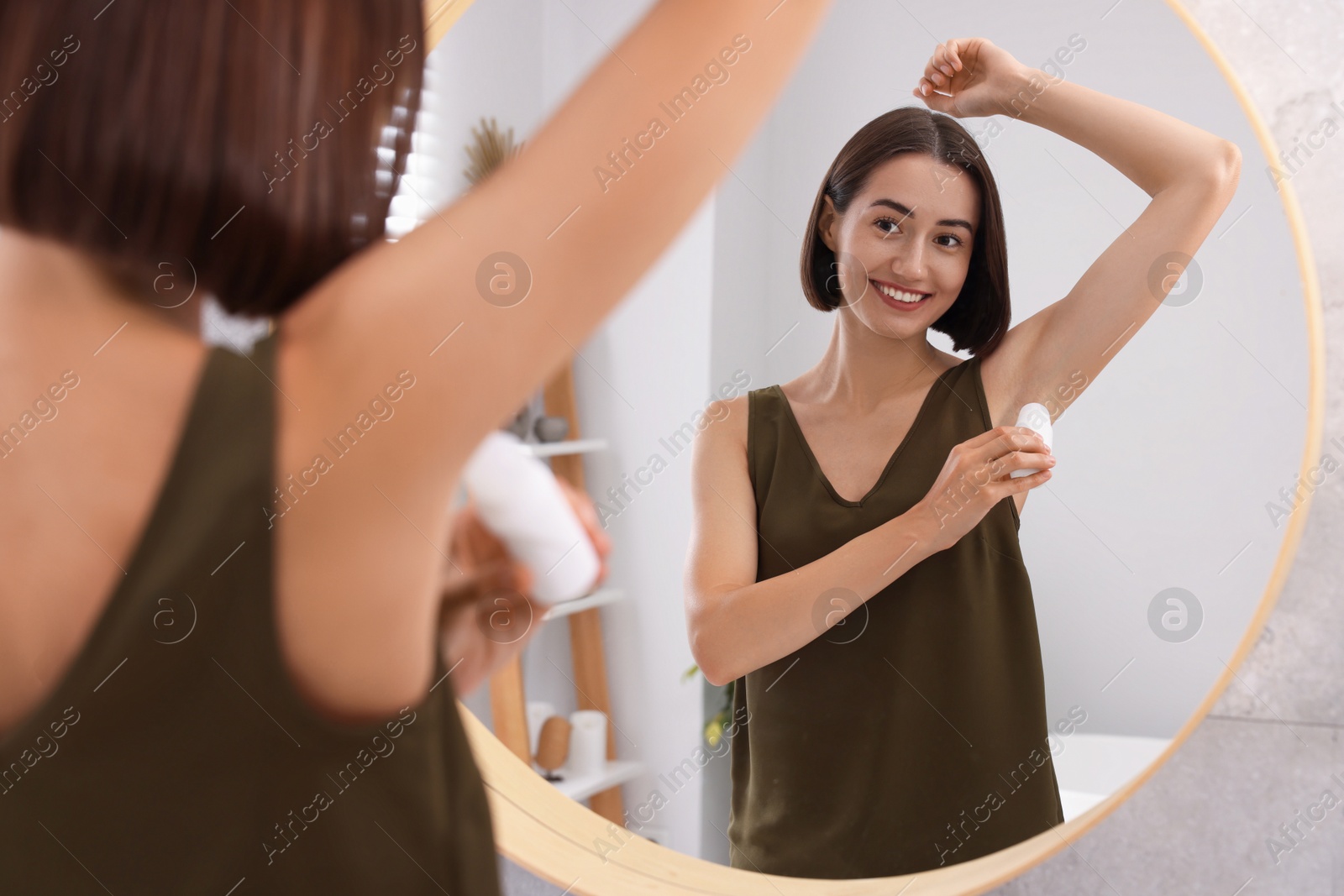 Photo of Smiling woman applying roll-on deodorant near mirror at home