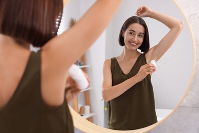 Photo of Smiling woman applying roll-on deodorant near mirror at home