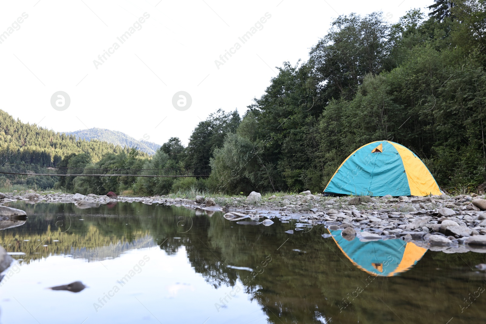 Photo of Camping tent on stones near river in mountains