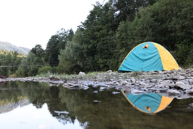 Camping tent on stones near river in mountains