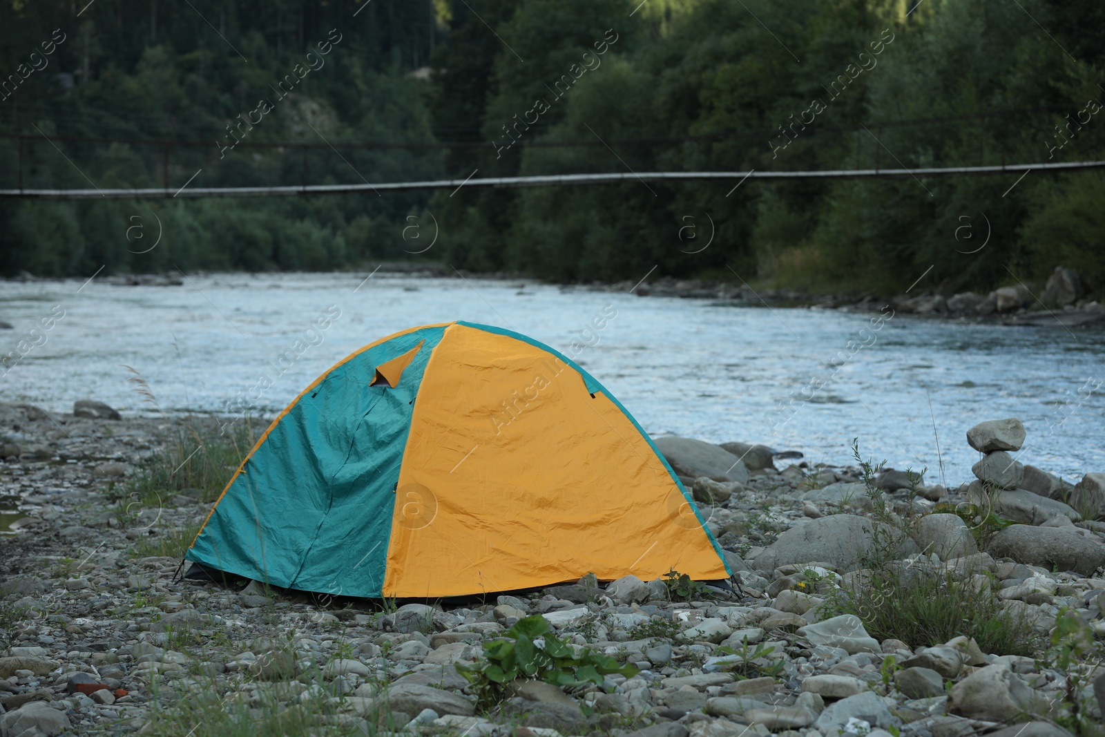 Photo of Camping tent on stones near river in mountains