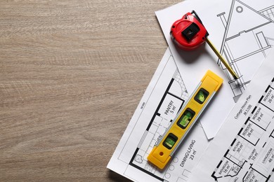 Photo of Different engineering drawings, building level and measuring tape on wooden table, flat lay. Space for text