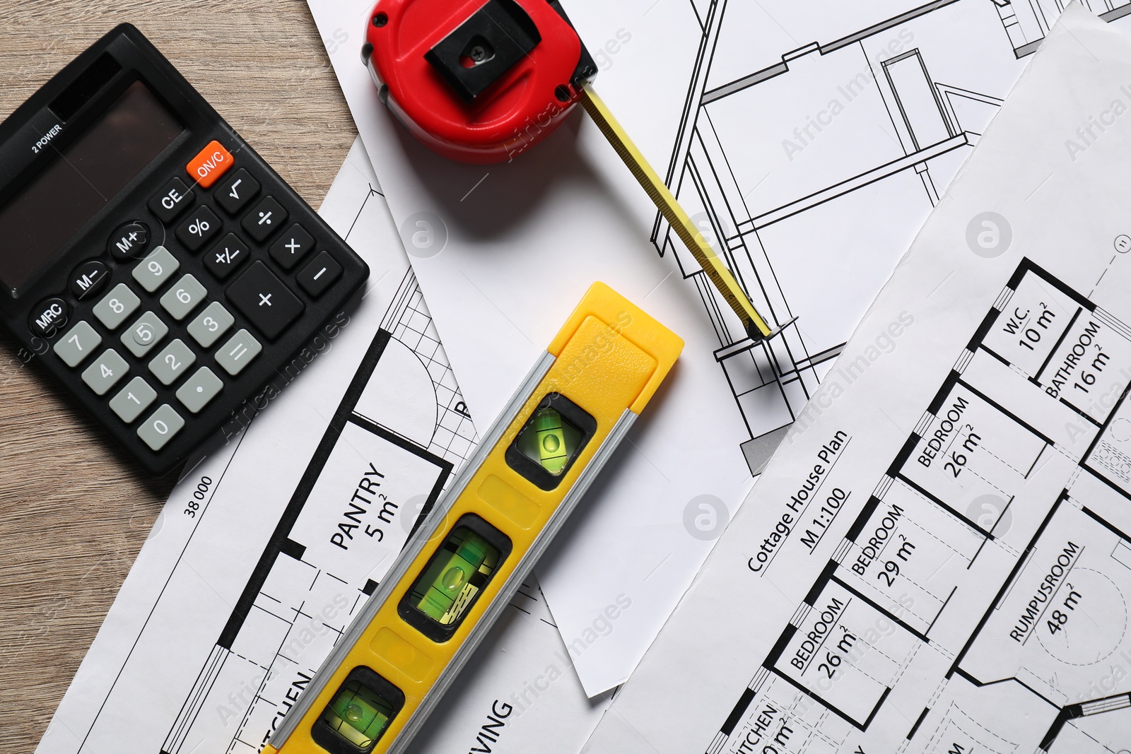 Photo of Different engineering drawings, calculator, building level and measuring tape on wooden table, flat lay