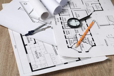 Photo of Different engineering drawings, dividers, pencil and magnifying glass on wooden table, closeup