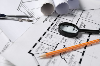 Photo of Dividers, pencil and magnifying glass on different engineering drawings, closeup