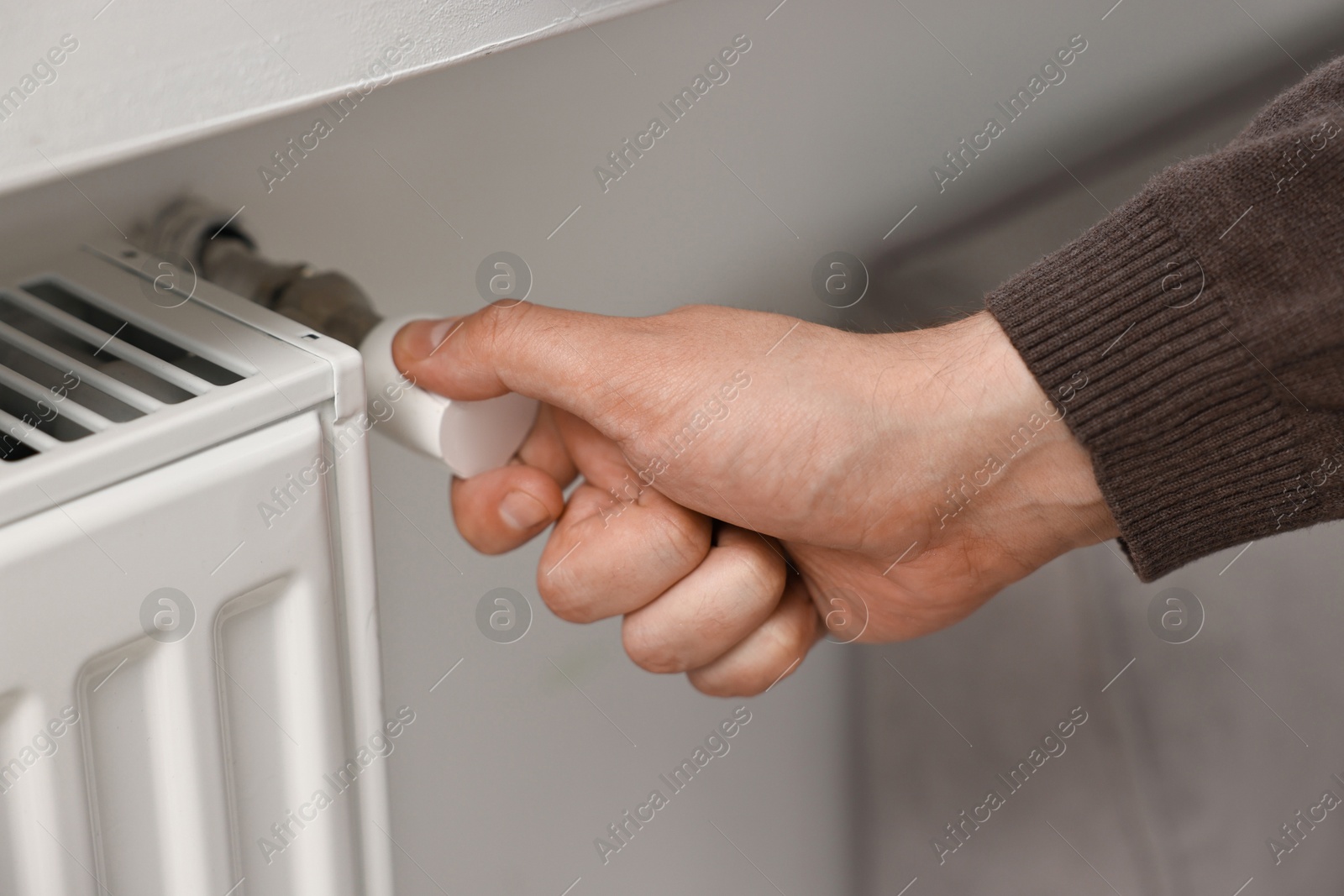 Photo of Man adjusting temperature of heating radiator indoors, closeup