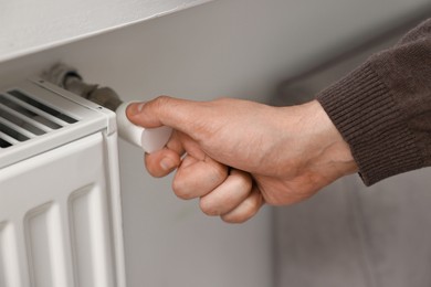 Photo of Man adjusting temperature of heating radiator indoors, closeup