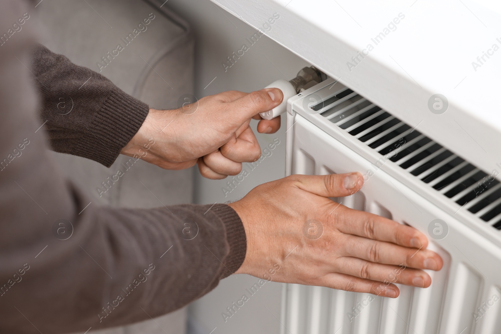 Photo of Man adjusting temperature of heating radiator indoors, closeup