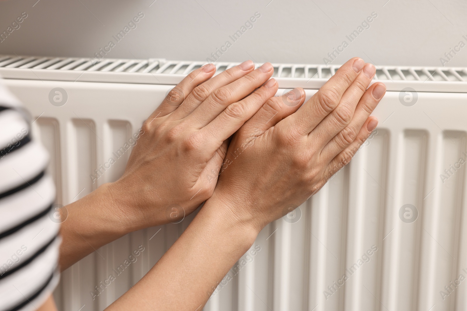 Photo of Woman warming hands near heating radiator indoors, closeup