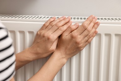 Photo of Woman warming hands near heating radiator indoors, closeup