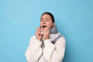 Sick woman with tissue sneezing on light blue background. Cold symptoms