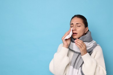 Sick woman with tissue on light blue background, space for text. Cold symptoms