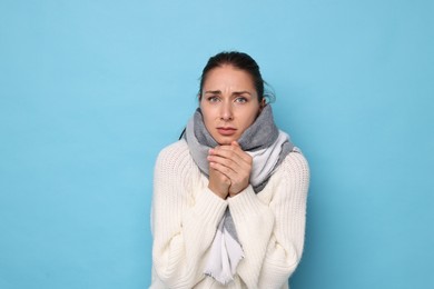 Sick woman suffering from cold symptoms on light blue background