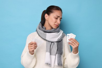 Sick woman with tissue and pills on light blue background. Cold symptoms