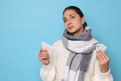 Sick woman with tissue and pills on light blue background. Cold symptoms