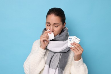 Sick woman with tissue and pills on light blue background. Cold symptoms