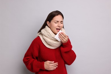 Sick woman with tissue sneezing on grey background. Cold symptoms