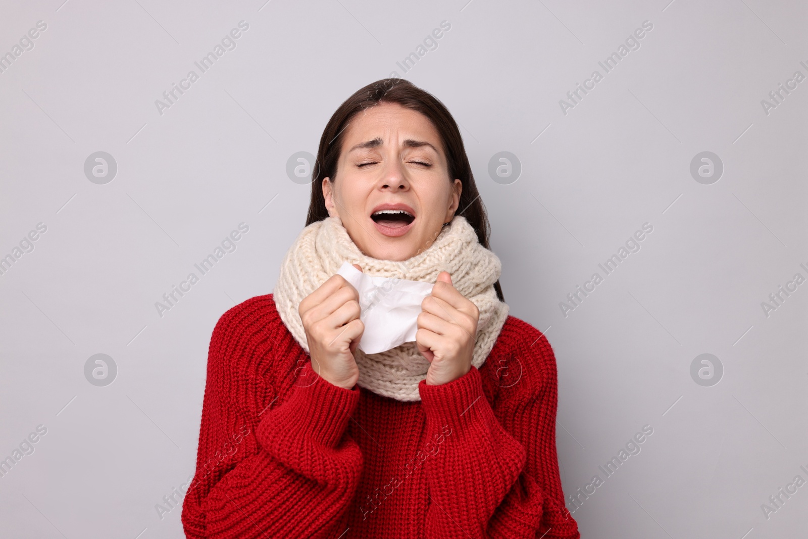 Photo of Sick woman with tissue sneezing on grey background. Cold symptoms