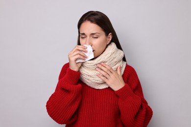 Photo of Sick woman with tissue on grey background. Cold symptoms