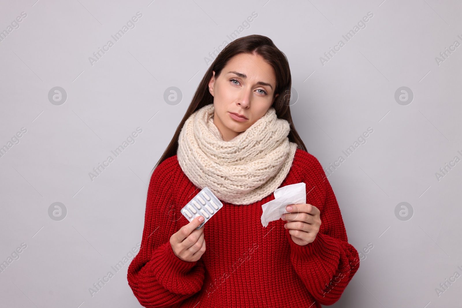 Photo of Sick woman with tissue and pills on grey background. Cold symptoms