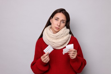 Photo of Sick woman with tissue and pills on grey background. Cold symptoms