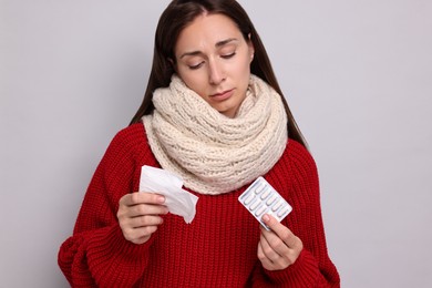 Sick woman with tissue and pills on grey background. Cold symptoms