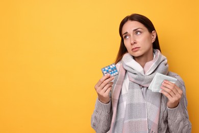 Sick woman with tissue and pills on orange background, space for text. Cold symptoms