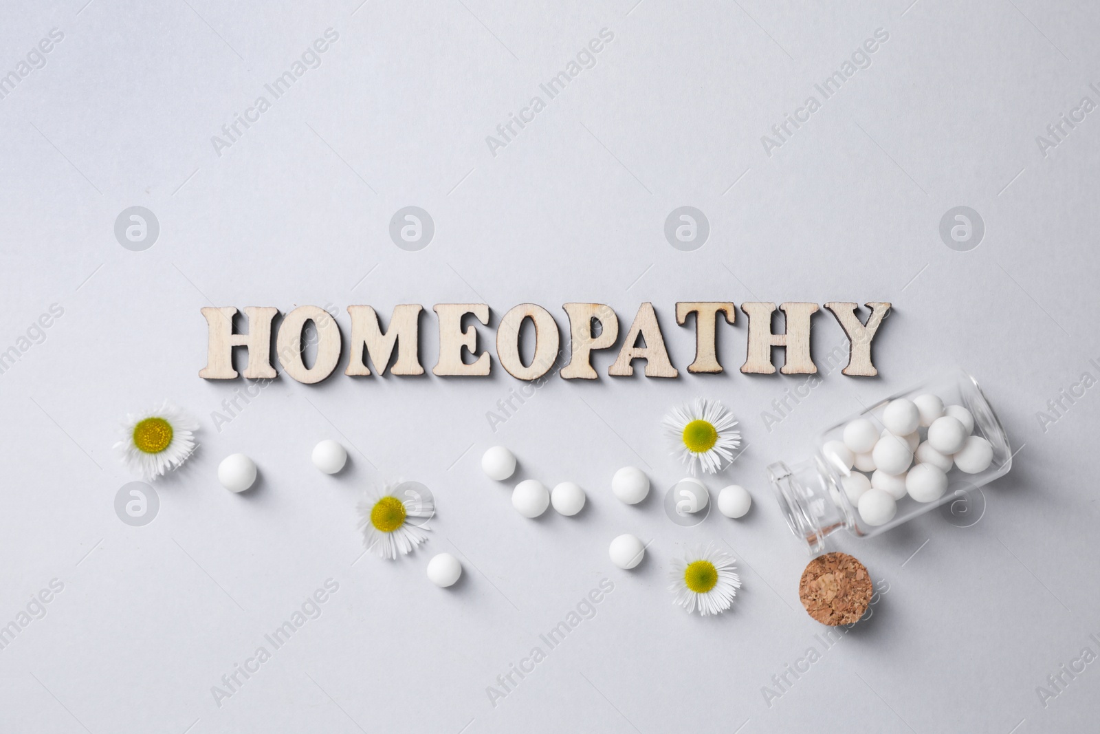 Photo of Word Homeopathy, chamomile flowers and pills on white background, flat lay