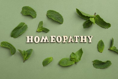 Photo of Word Homeopathy and mint leaves on green background, flat lay