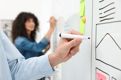 Photo of Developing UI design. Man and woman drawing website wireframe on whiteboard indoors, selective focus