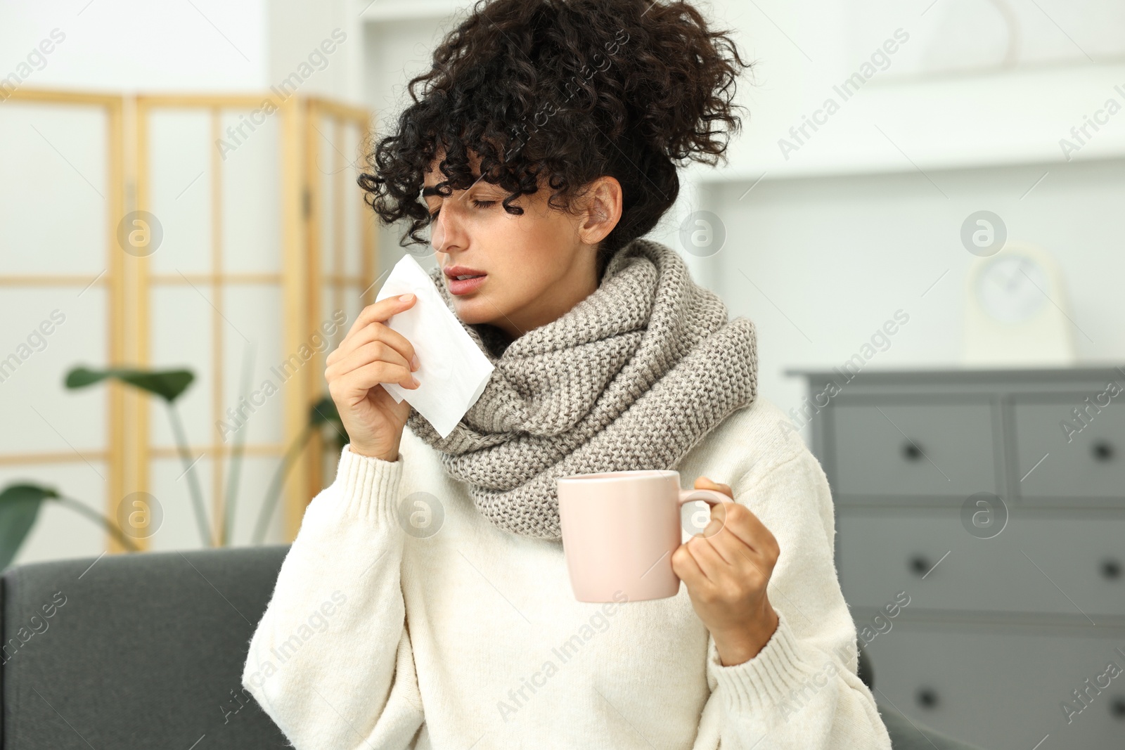 Photo of Cold symptom. Young woman with tissue and cup of hot drink at home