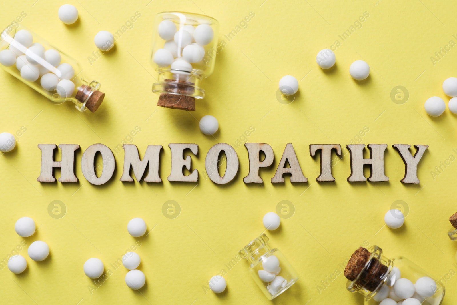 Photo of Word Homeopathy and pills on pale yellow background, flat lay