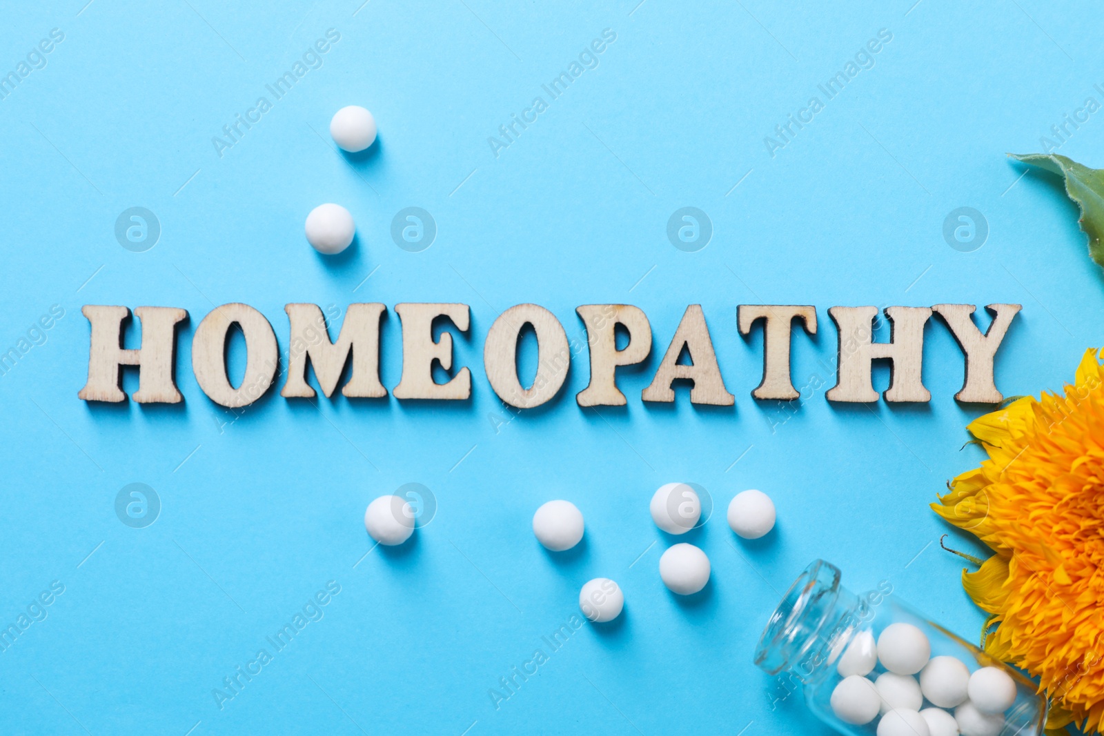 Photo of Word Homeopathy, pills and flower on light blue background, flat lay