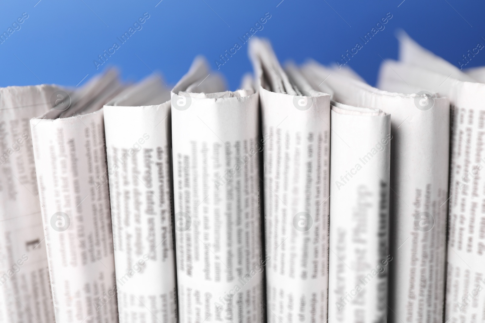 Photo of Many newspapers in different languages on blue background, closeup