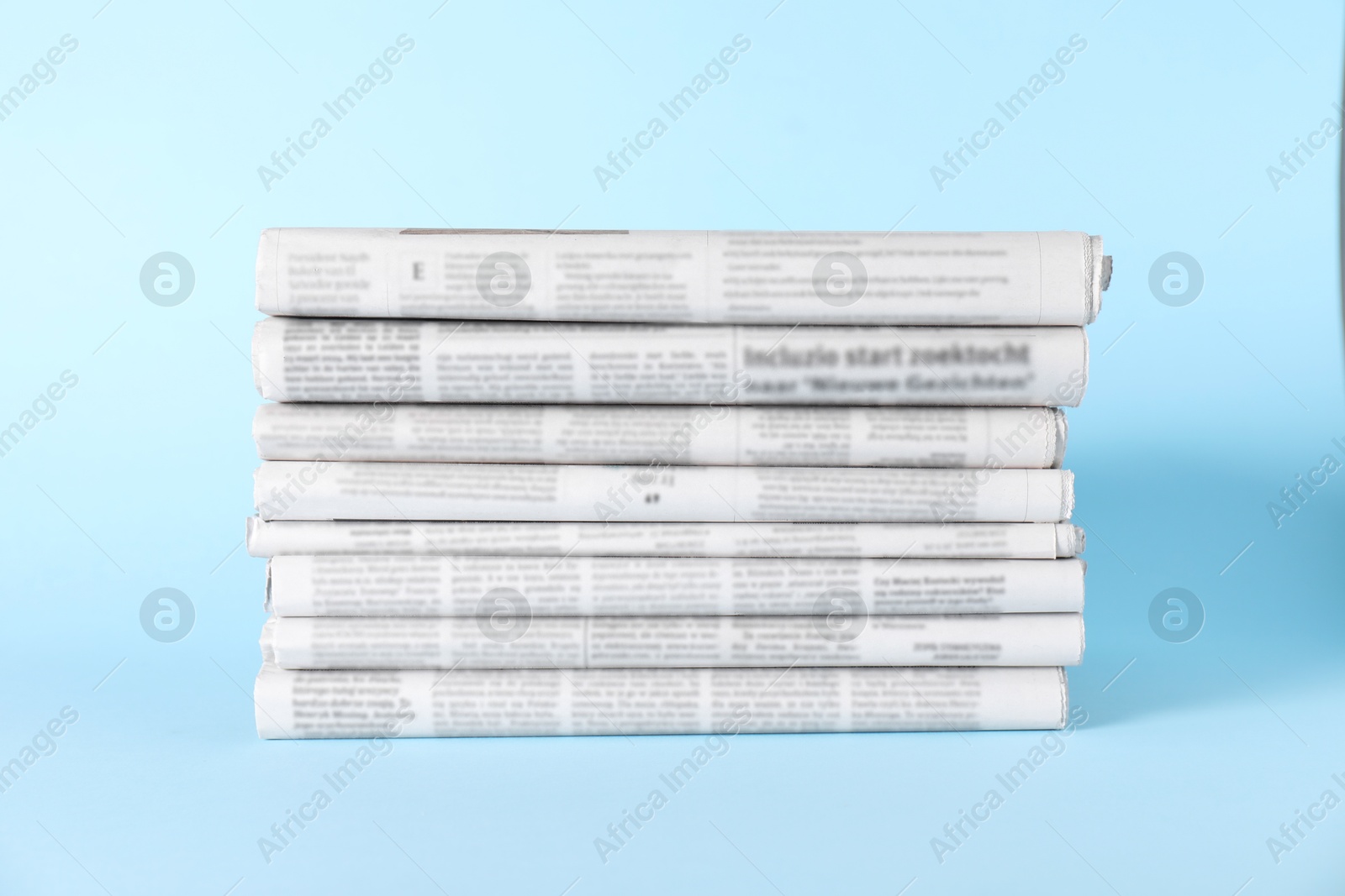 Photo of Stack of newspapers in different languages on light blue background