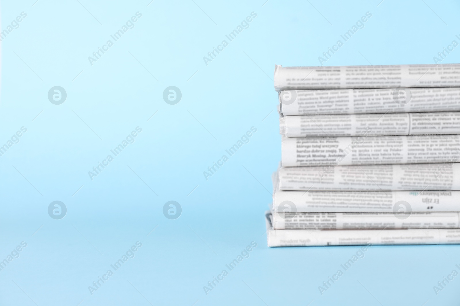 Photo of Stack of newspapers in different languages on light blue background, space for text