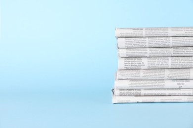 Stack of newspapers in different languages on light blue background, space for text