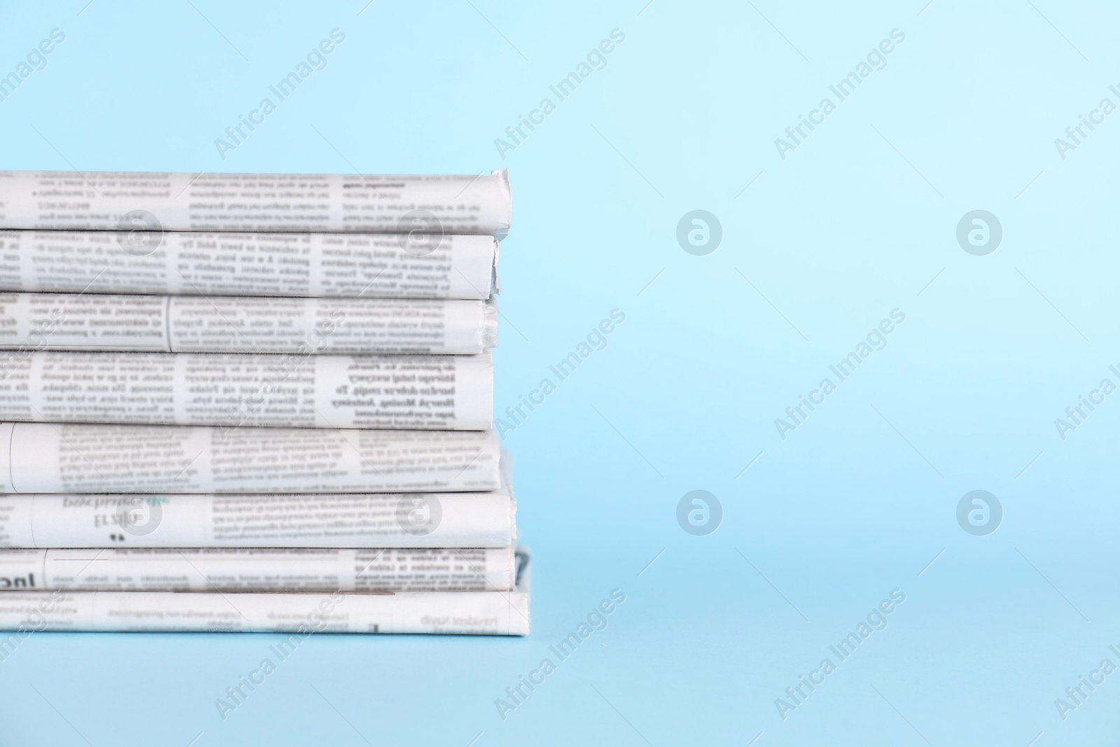 Photo of Stack of newspapers in different languages on light blue background, space for text