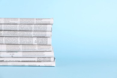 Photo of Stack of newspapers in different languages on light blue background, space for text