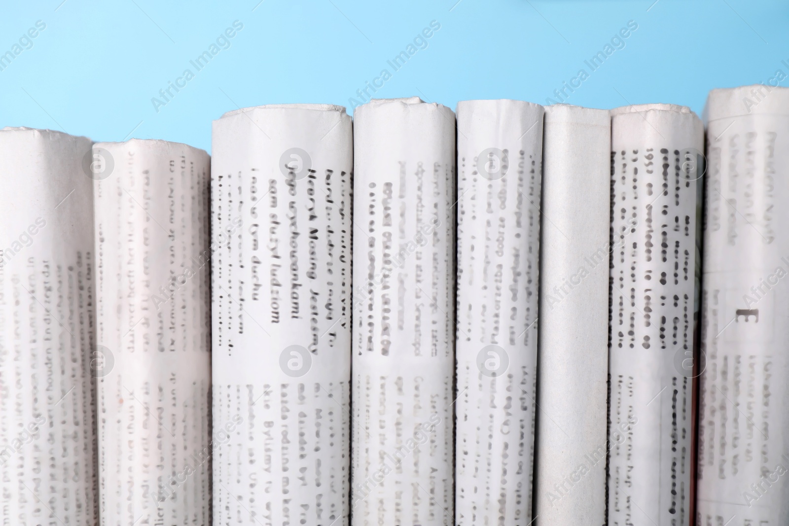 Photo of Many newspapers in different languages on light blue background, closeup