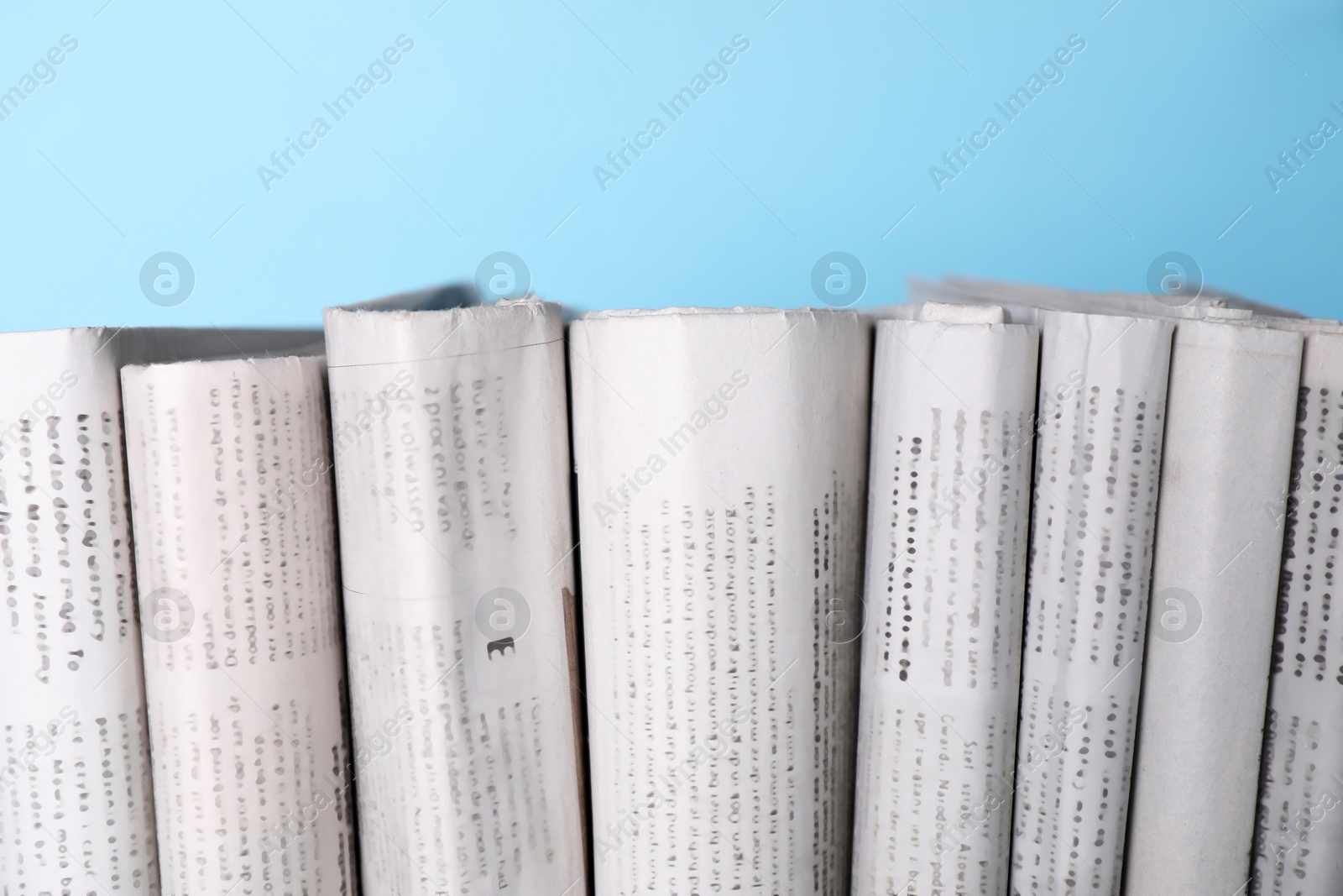 Photo of Many newspapers in different languages on light blue background, closeup