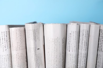 Many newspapers in different languages on light blue background, closeup