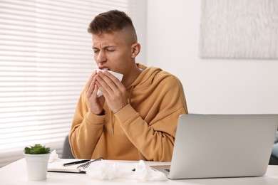 Photo of Cold symptom. Young man sneezing at desk indoors