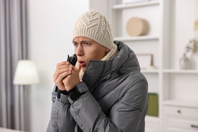 Cold symptom. Young man in winter coat coughing at home