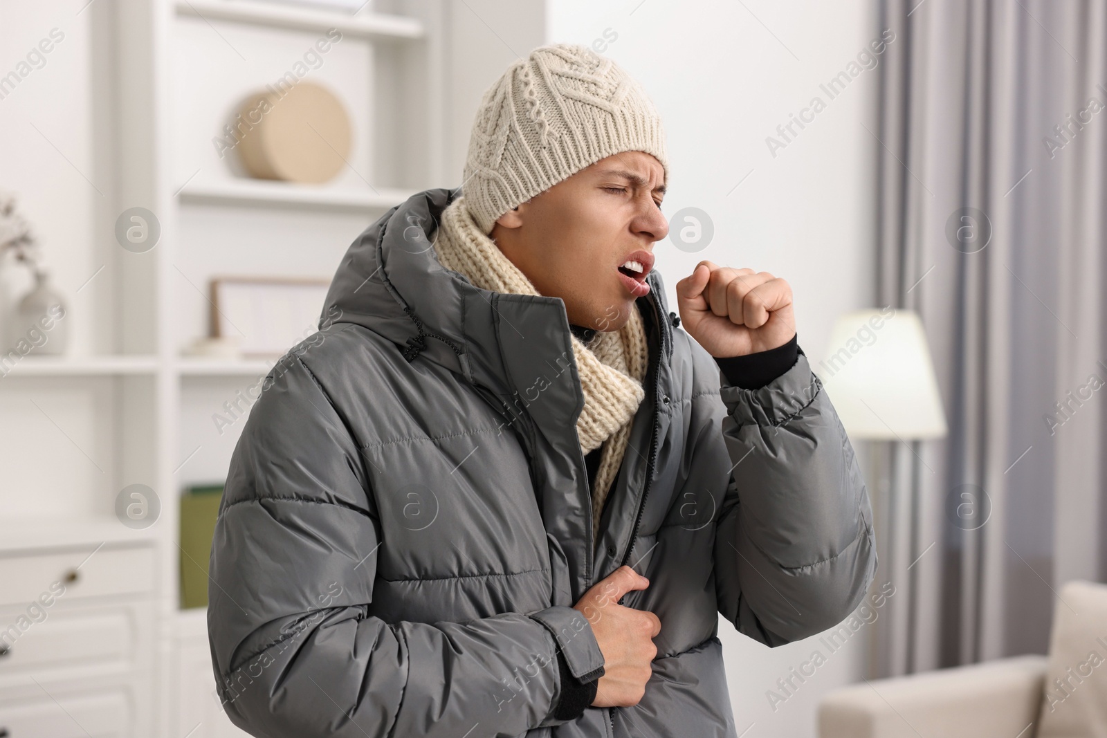 Photo of Cold symptom. Young man in winter coat coughing at home