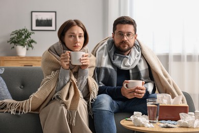 Cold symptom. Couple with cups of drink suffering from fever on sofa at home