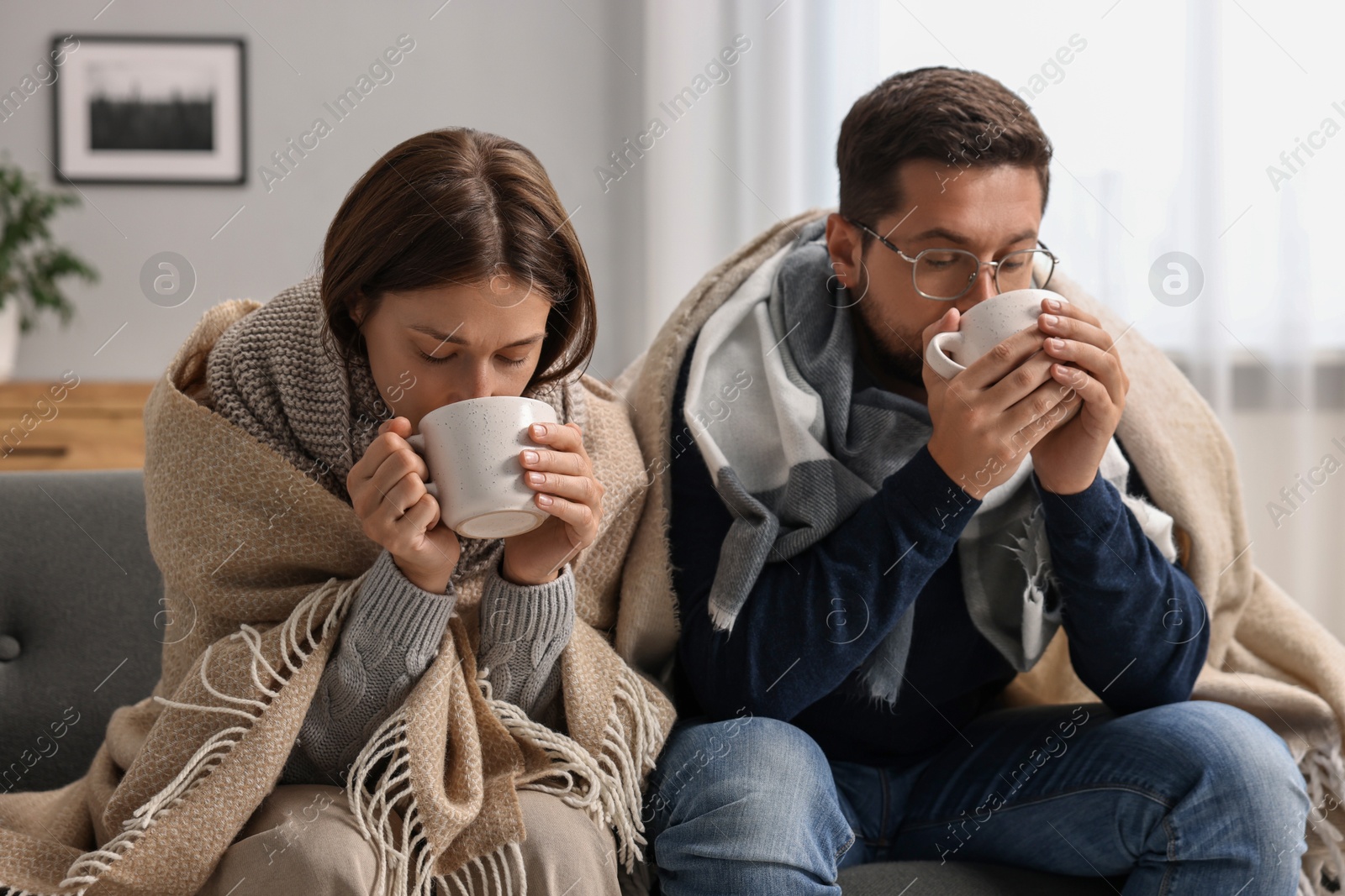 Photo of Cold symptom. Couple with cups of drink suffering from fever on sofa at home