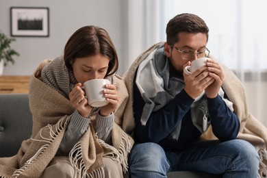 Photo of Cold symptom. Couple with cups of drink suffering from fever on sofa at home