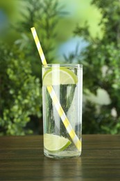 Photo of Glass of soda water with lime on wooden table against blurred background