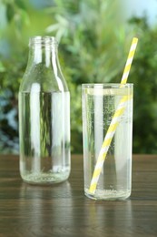 Photo of Glass and bottle of soda water with lime on wooden table against blurred background